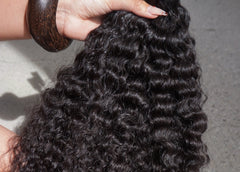 Close-up of a hand holding a curl of black hair against a neutral background