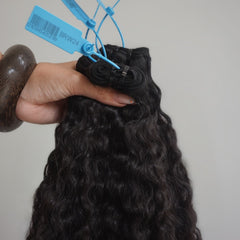 Black hair extensions held by a hand with a blue tag on a gray background
